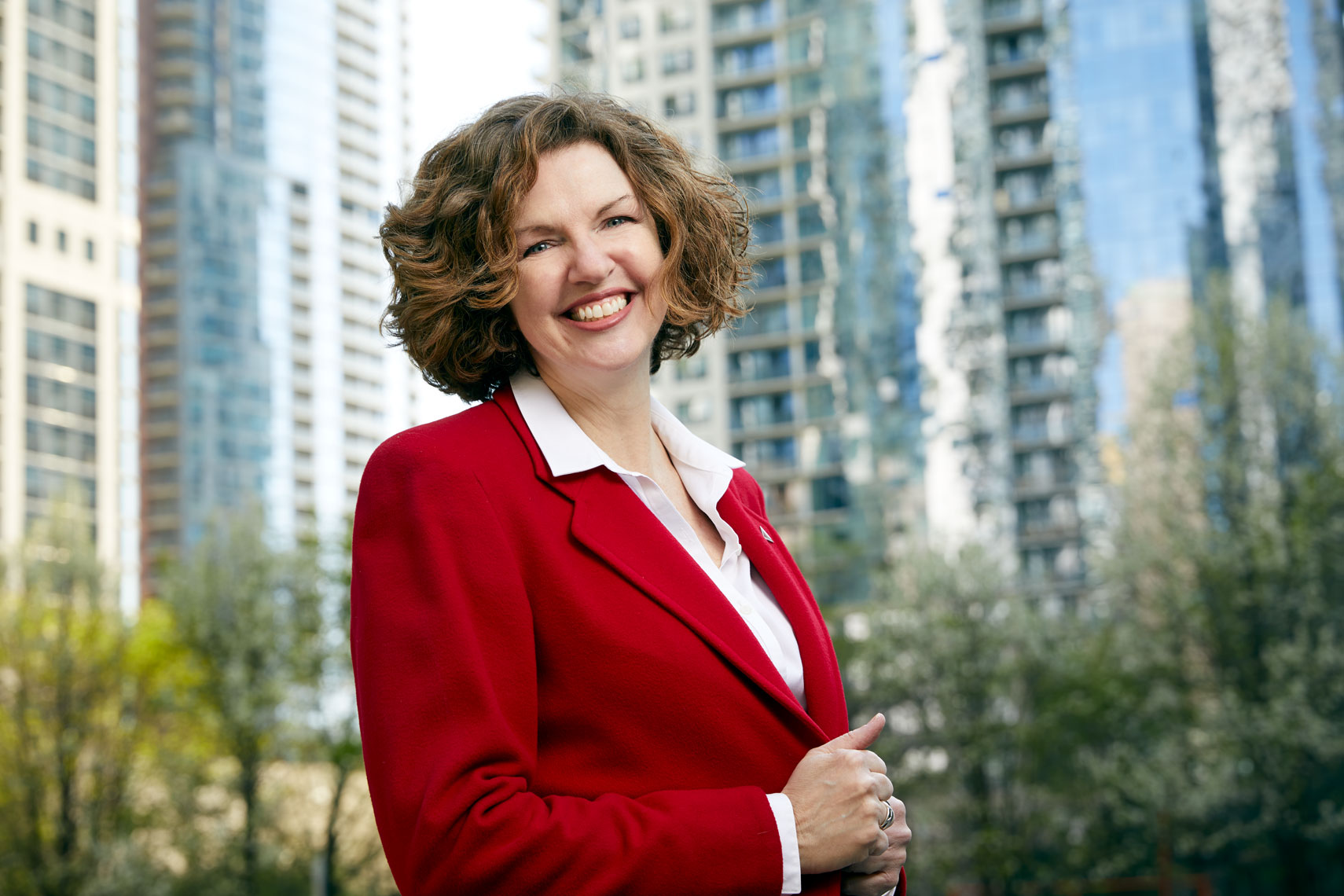 Smiling woman in urban setting wearing a red jacket. 