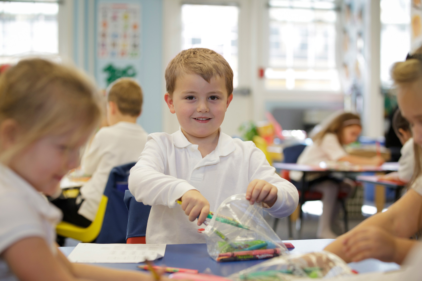 Kindergarten boy in white shirt with crayons in school.