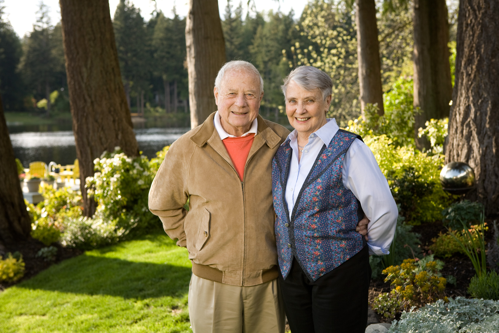 Couple standing in backyard with late afternoon light and large trees.